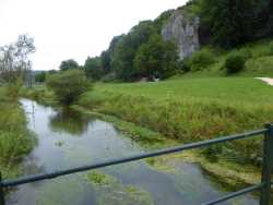 Von der Brücke über die langsam fließende Ach schaut man auf die Felsen und den