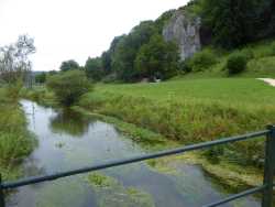 Von der Brücke über die langsam fließende Ach schaut man auf die Felsen und den 