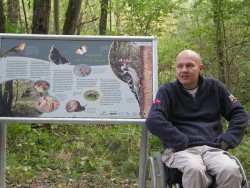 Eine Infotafel des Naturlehrpfades am Wegesrand. Geislingens Behindertenbeauftragter Michael Schima blickt zufrieden in die Kamera.