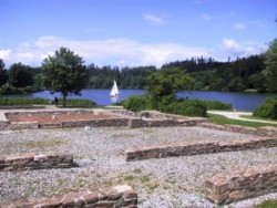 im Vordergrund die Mauerreste des ehemaligen Römerbades. Im Hintergrund ein Segelboot auf dem See.