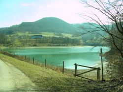 von der Dammkrone aus öffnet sich der Blick über den Stausee in Richtung zum bewaldeten Grasberg und unterhalb davon das Stausee-Hotel.