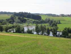 Von Aichstrut kommend, öffnet sich der Blick auf den Aichstrutsee. Er liegt eingebettet zwischen Wiesen in einer Hügellandschaft.